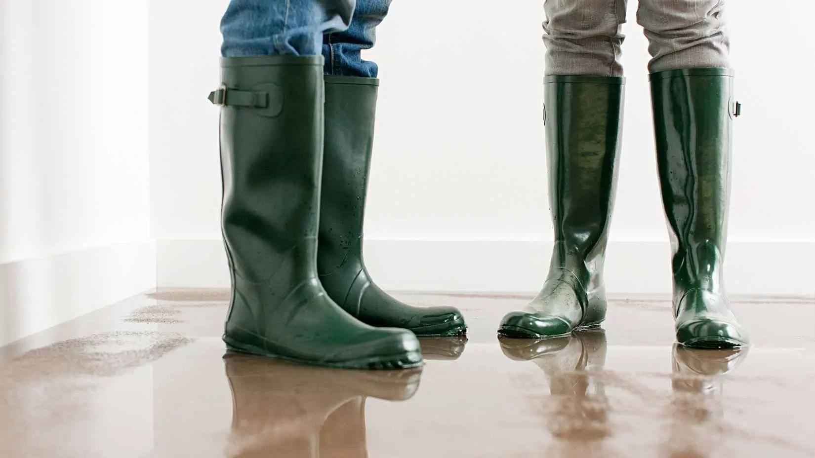 Two people wearing green rubber boots standing on a wet floor.